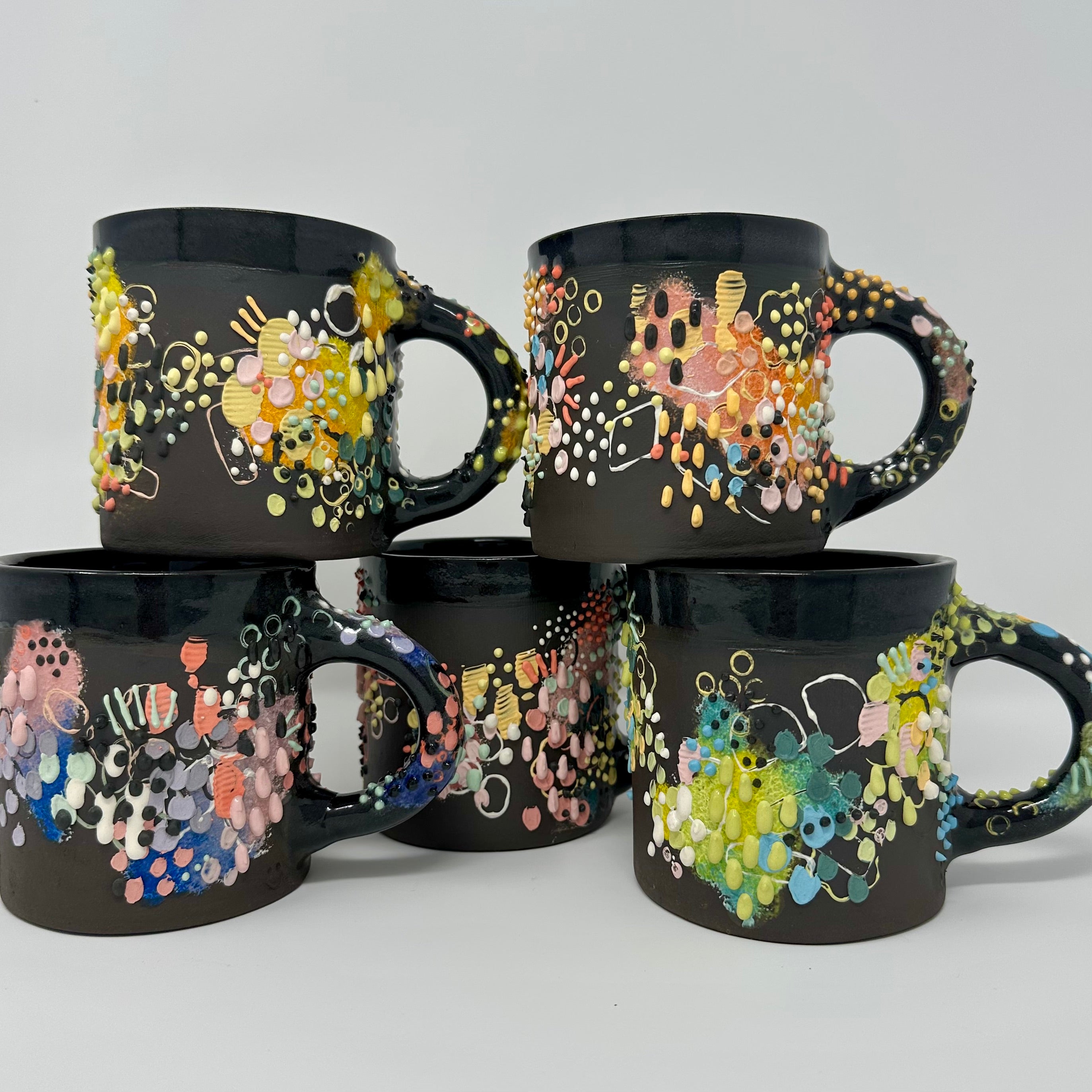 Five black decorative coffee mugs with colorful designs on a white background