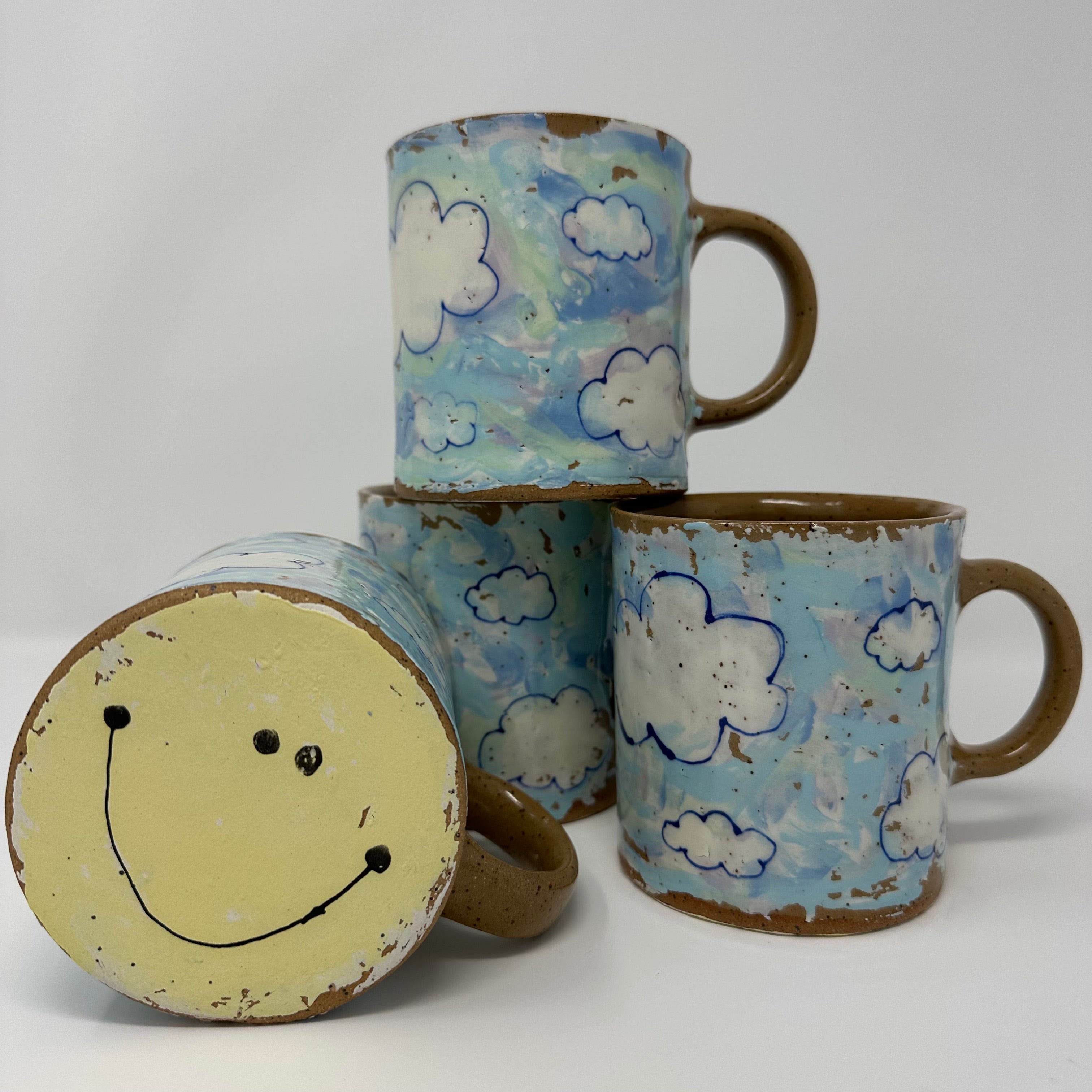 Ceramic coffee mugs decorated with clouds and smiley faces