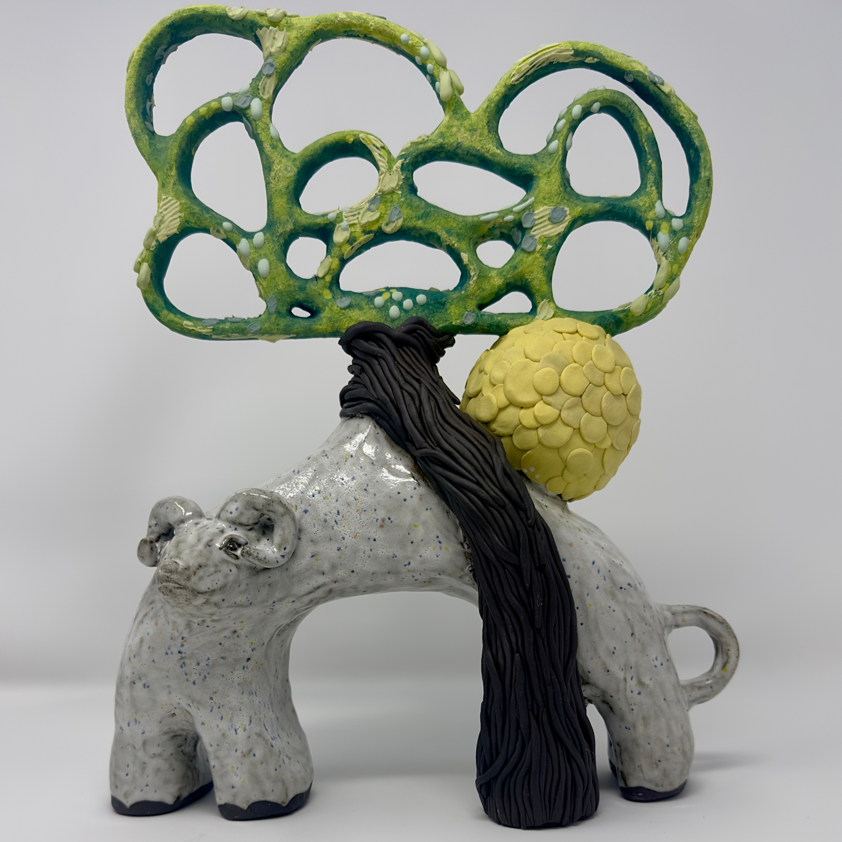 Ceramic sculpture with green abstract design, gray base, yellow sphere, and black thread on a white background